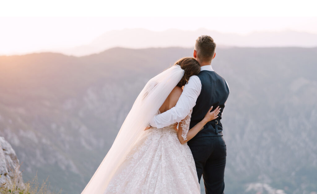 Bride resting shoulder on groom's shoulder as they look over valley